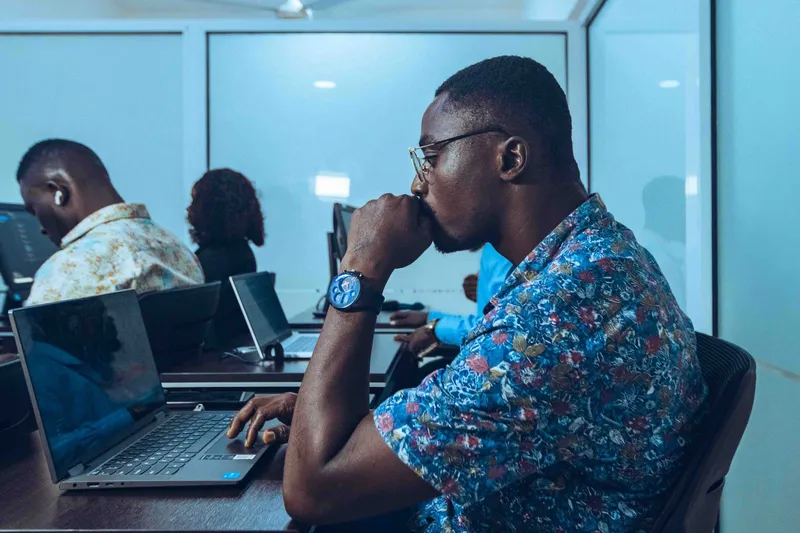 Adult learners working at laptops during an IT workshop in Accra, Ghana.